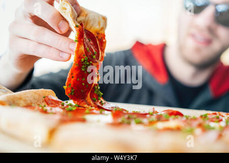 Young attractive smiling man eating pizza at street cafe. Cheat meal. Cheat day. Stock Photo