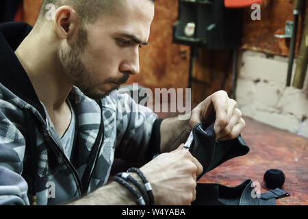 Craftsman intently works with leather. Tanner sews leather goods. Making handmade stuff. Male hands with needle and thread. Man working with needle an Stock Photo