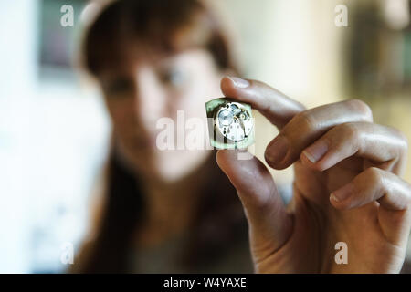 Portrait of woman watchmaker. Girl with blurred face holds clock in hand. Clockwork in fingers. Gears in disassembled watches on blurred background. Stock Photo