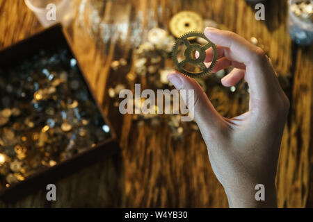 Watchmaker holds large gear. Cogwheel on blurred background of workplace. Pinion in female hand. Old cogwheel on wooden table background. Big metal ge Stock Photo