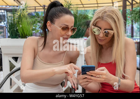 Girls siting in cafe or restaurant and look at mobile phone, taking selfie Stock Photo