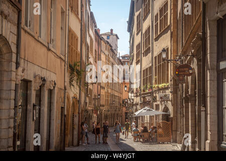 LYON, FRANCE - JULY 14, 2019: Typical narrow street of the Vieux Lyon (old Lyon) on the Presqu'ile district with tourists passing by during a sunny su Stock Photo