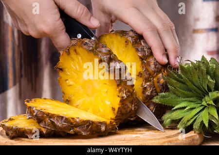 hands cutting pineapple on a cutting board, closeup Stock Photo
