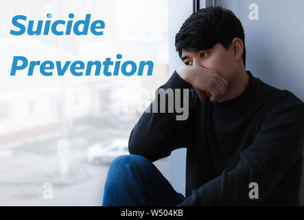 Depressed Asian man sitting near window. Suicide prevention concept Stock Photo