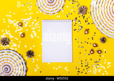 Christmas decorations and sparkles on yellow background. Blank notepad with place for your text. Stock Photo