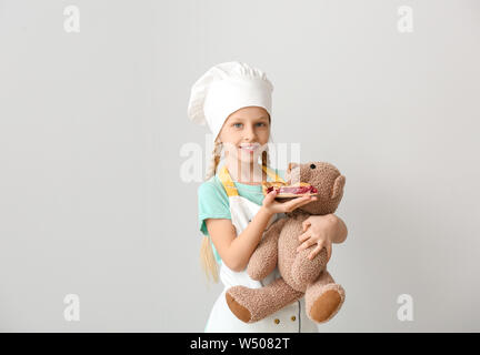 Cute little chef feeding toy bear with piece of pie on white background Stock Photo