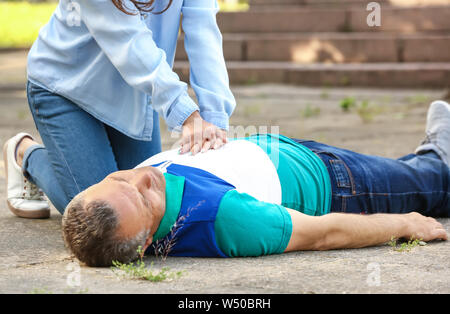 Female passer-by doing CPR on unconscious mature man outdoors Stock Photo