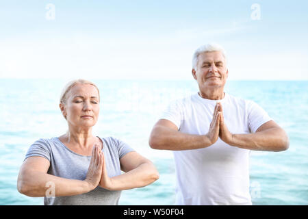 Mature couple practicing yoga at sea resort Stock Photo