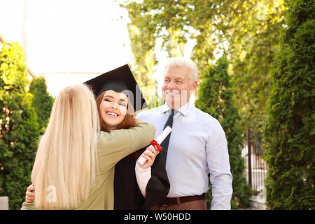 Happy young woman with diploma and her parents on graduation day Stock Photo