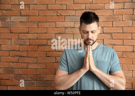 Religious man praying against brick wall Stock Photo