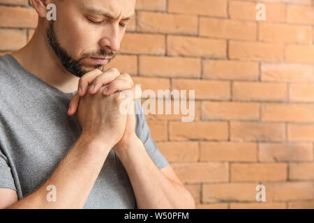 Religious man praying against brick wall Stock Photo