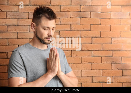 Religious man praying against brick wall Stock Photo