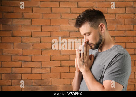 Religious man praying against brick wall Stock Photo