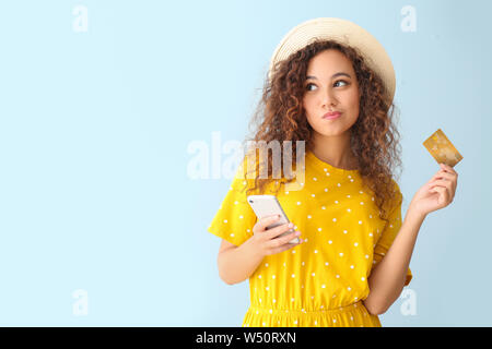 Thoughtful African-American woman with credit card and mobile phone on light color background Stock Photo