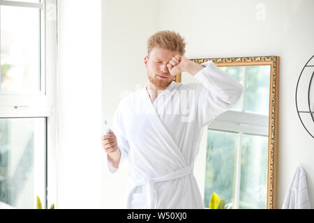 Morning of sleepy young man with toothbrush in bathroom Stock Photo