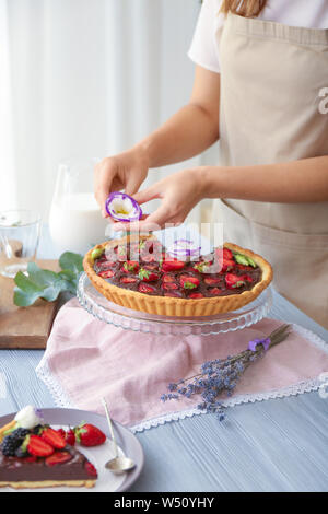 Woman decorating tasty chocolate strawberry cake with flower Stock Photo