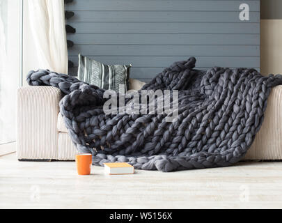 Merino wool grey blanket lying on white sofa with an orange cup and book near it Stock Photo