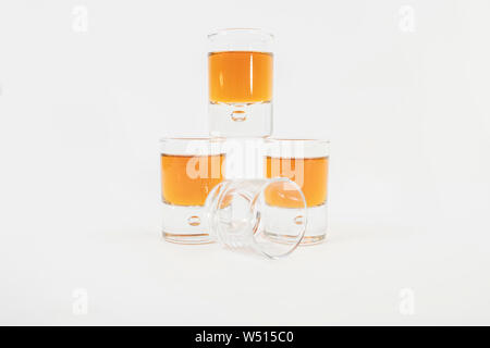 Three small glasses filled with luxurious whiskey next to an empty glass, isolated on a white background - Close-up Stock Photo