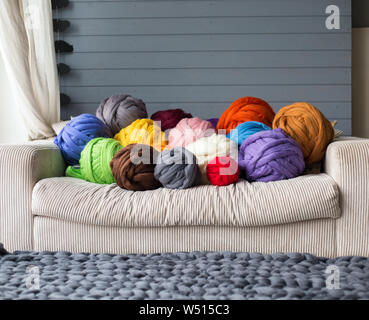 Merino wool balls in multicolour lying on white sofa with merino wool grey blanket on a floor Stock Photo