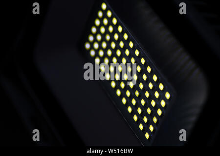A rectangular diode spotlight of gray color in a dark room illuminates with yellow light. Blurred background Stock Photo