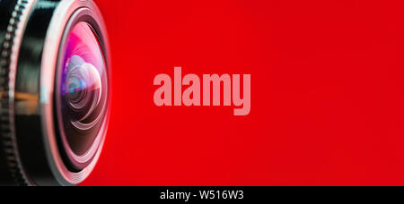 Banner. Camera lens with red backlight. Side view of the lens of camera on red background. Red  camera Lens close Up. Optics Stock Photo