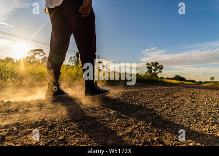 Man wearing sneakers walking along railway path on sandy and dusty road on sunny afternoon Stock Photo