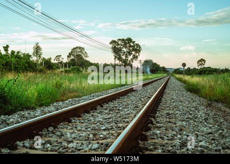 Railway tracks with a green landscape with trees in Asia at sunset Stock Photo