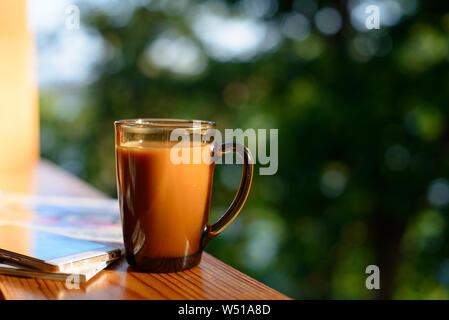 Cup of coffee and cellphone on the windowsill over blurred forest background at sunny summer day. Free copy space. Stock Photo