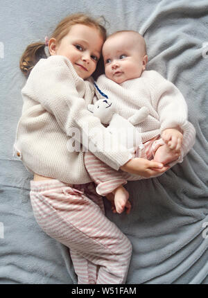 Lifestyle portrait of cute Caucasian girls sisters holding little baby on bed. Family love bonding together concept Stock Photo