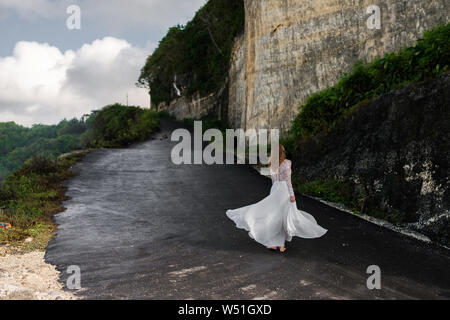 Bride dancing in white dress on cliff in Bali Stock Photo