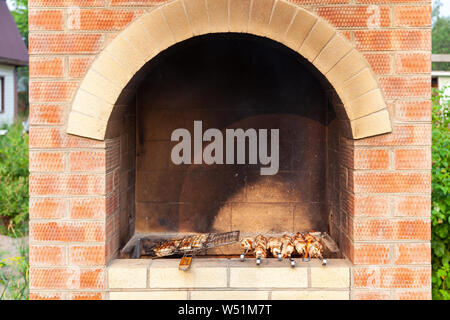 Close-up on the process of cooking barbecue of pork or beef meat mounted on skewers in a brick stove with a crispy burnt crust over gray burnt coals o Stock Photo