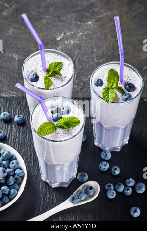 blueberry frothy smoothie of coconut milk in three glasses with straws on a black slate tray on a concrete table, vertical view from above Stock Photo
