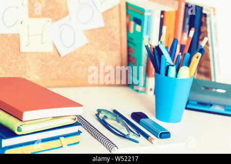 Back to school background. Stationery accessories – notebooks piles, plastic holder pencils, pens, markers, stickers, notepads, glasses and corkboard Stock Photo