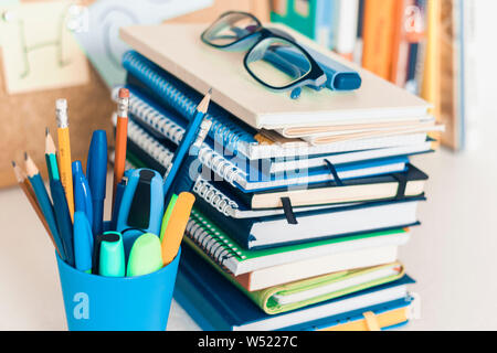 Back to school background. Stationery accessories – notebooks piles, plastic holder pencils, pens, markers, stickers, notepads, glasses and corkboard Stock Photo