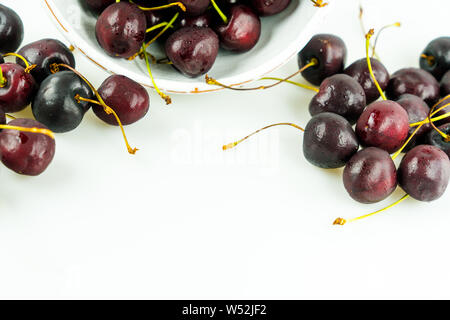 horizontal view of fresh organic ripe black cherries in a bowl and spread around on an isolated white background Stock Photo