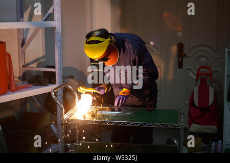 The father of Chinese Peppa Pig fan Han Bing performs welding on a partially-finished 'Iron Peppa' model at their workshop in Beijing, China, 22 Janua Stock Photo