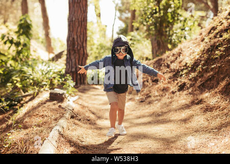 Cute boy with pilot goggles and hat running in forest. Kid pretending to be pilot playing in forest. Stock Photo