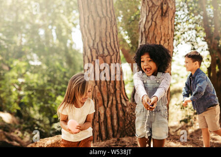 Girls bursting water balloons with hands in a park. Group of kids having fun in forest. Stock Photo