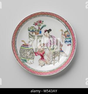 Saucer with a Chinese lady, boy and rabbit, Porcelain dish, painted on the glaze in blue, red, pink, green, yellow, purple, black and gold. On the plate of the dish a Chinese lady on a chair with next to her a boy with a rabbit in front of him, they are surrounded by lucky objects such as a dragon vase, coral and peacock feather vase, flower vase, fruit basket, incense burner and a vase with scrolls, the inner edge with a decorative band with napkin work. Dish has been broken. Famille rose., anonymous, China, c. 1725 - c. 1749, Qing-dynasty (1644-1912) / Yongzheng-period (1723-1735) / Qing Stock Photo