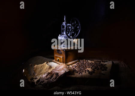 Stylized vintage coffee grinder on a wooden table sprinkled with coffee beans and dry leaves. Stock Photo
