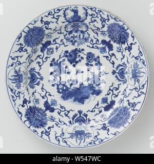 Dish Dish with the arms of the Pelgrom family, Porcelain dish, painted in underglaze blue. On the shelf a bird on a rock with flowering plants (peony). On the wall and border alternately large lotus vines and a lobed cartouche with a stylized flowering plant. In between the coat of arms of the Pelgrom family surrounded by acanthus leaves and an Asian figure as a helmet sign. Weapon porcelain in blue and white, flowers, ornament, Bengal, Jacob Pelgrom, anonymous, China, c. 1680 - c. 1699, Qing-dynasty (1644-1912) / Kangxi-period (1662-1722), porcelain (material), glaze, cobalt (mineral Stock Photo
