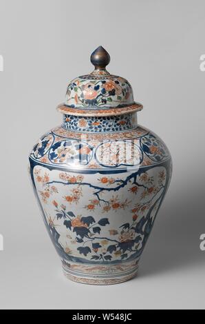 Covered jar with flowering plants in panels, flower sprays and scrolls, Baluster-shaped porcelain covered pot, painted in underglaze blue and on the enamel red, green and gold. On the belly four large, scalloped cartouches with flowering plants (prunus, peony, grasses) near rocks. On the shoulder a band with lobed cartouches with flower sprays (chrysanthemum, prunus, peony), half flower rosettes with three leaves between the cartouches. A band with floral scrolls around the neck and foot. Flower vines on the neck. The foot with a band curl. Imari., anonymous, Japan, c. 1700 - c. 1749, Edo Stock Photo