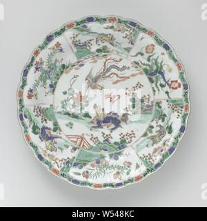 Dish with mythological animals in landscapes, Porcelain dish with ribbed wall and lobed edge, painted in underglaze blue and on the glaze blue, red, green, yellow, eggplant, black and gold. On the flat a double medallion with a flying feng huang above a qilin in a landscape with a fence, rocks, flowering plants and clouds. Around the medallion on the wall six compartments with alternating flowering plants near a rock (beautiful carnation, aster) and mythological animals in a landscape (shishi / lion dog). On the edge a band with floral scrolls. The outer wall with three flower sprays. Marked Stock Photo
