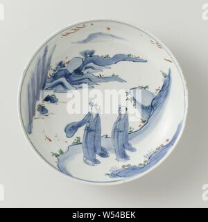 Saucer dish with Chinese figures in a landscape, Porcelain dish, painted in underglaze blue and on the enamel red, green, yellow and black. On the shelf two Chinese people (hermits) in a landscape with mountains and trees. The outer wall with three times a pearl with four dots. Marked on the bottom with the four-character mark of emperor Tianqi in a double circle. Baking sand on the foot ring. Ko-sometsuke., Standing figure, anonymous, China, c. 1621 - c. 1627, Ming-dynasty (1368-1644) / Tianqi-period (1621-1627), porcelain (material), glaze, cobalt (mineral), vitrification, h 4.5 cm d 20.8 cm Stock Photo