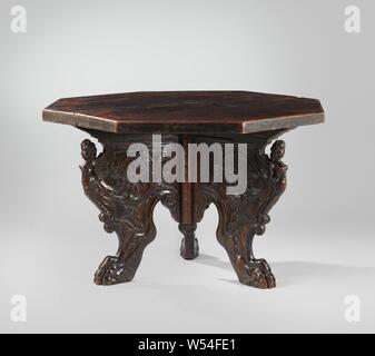 Octagonal table, Latafel made of poplar wood with an octagonal, unadorned and unprofiled top, standing on three cheek legs, ending in claws. The cheek legs show a winged female figure on the knee, whose lower body ends in a volute. From under her wings a relief-carved rank volume emerges, in which various mythical creatures. The claws end up in an acanthus leaf on the outside and a volute on the inside, with a flower in between., anonymous, Italy, 1500 - 1600, poplar (wood), walnut (hardwood), h 77 cm × d 129 cm Stock Photo
