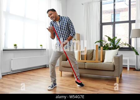 man with broom cleaning and singing at home Stock Photo