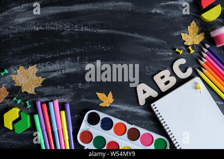 Back to school concept. Notebook, colored pencils, gouache, watercolor and dried maple leaves and office supplies on black table background. Flat lay, Stock Photo