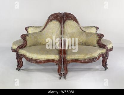 Armchair, part of an environmental divan, Armchair belonging to a set of six armchairs made of mahogany with a triangular base, forming a round sofa. Floral silk trim with trimmings. The two angled placed front legs, the rear leg, lines, struts, armrests and the crown of the backrest are bent, profiled and almost all end up in a volute. The armrests close the backrest in an arched shape and form a triangular crown that, like the fore-end and the swellings of the front legs, has shell-shaped acanthus leaves., Gebroeders Horrix, The Hague, c. 1852, wood (plant material), mahogany (wood), silk Stock Photo