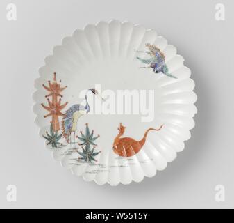 Fluted saucer-dish with cranes, minogame and pine shoots, Porcelain dish with a ribbed wall and lobed edge, painted on the glaze in blue, red, green, yellow, black and gold. On the shelf a standing crane among pine shoots, watching a mini game on the ground. A second crane in the air. A few chips in the edge. Arita, Kakiemon., anonymous, Japan, c. 1670 - c. 1690, Edo-period (1600-1868), porcelain (material), glaze, gold (metal), vitrification, h 3.9 cm d 24.5 cm Stock Photo