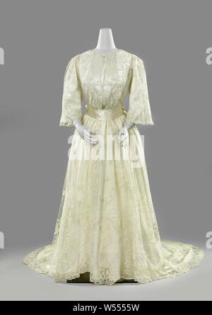 Lace wedding dress, Wedding gown from application side with garden trophies in medallions, Tailored drag dress from Brussels application side, with closure. The body has a high round neck, shoulder flaps and three-quarter pagoda sleeves. The skirt is clocking, has a split on the front and a round trail. The motifs are made from bobbin lace with needle lace decorative stitches - Brussels duchesse - that is appliqued on machine tulle. The neck line is a bow with a 'garden trophy' consisting of a garden hat, shepherd's staff and rake. This 'trophy' is repeated in the five large medallions along Stock Photo